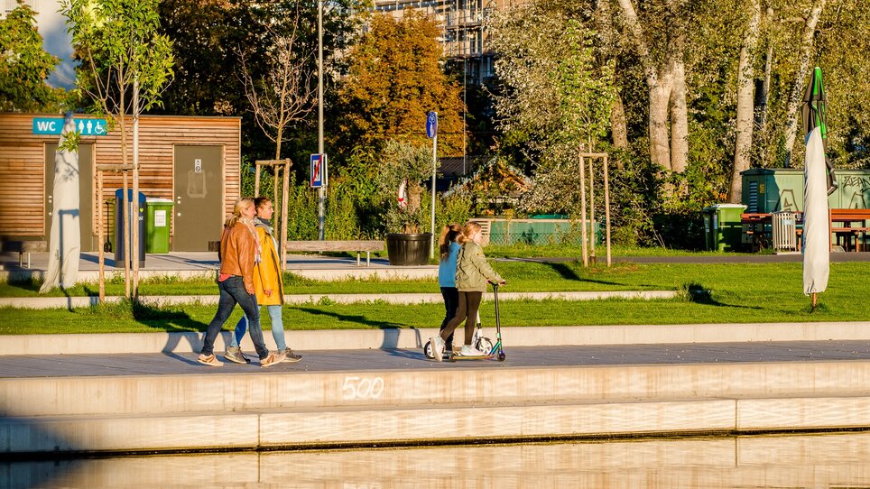 Two women are walking along the banks of the Mur with two girls on scooters. | © Graz Tourismus