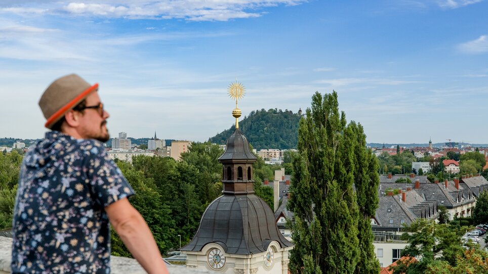 Mann blickt über Graz mit dem Grazer Schlossberg im Hintergrund. | © Graz Tourismus