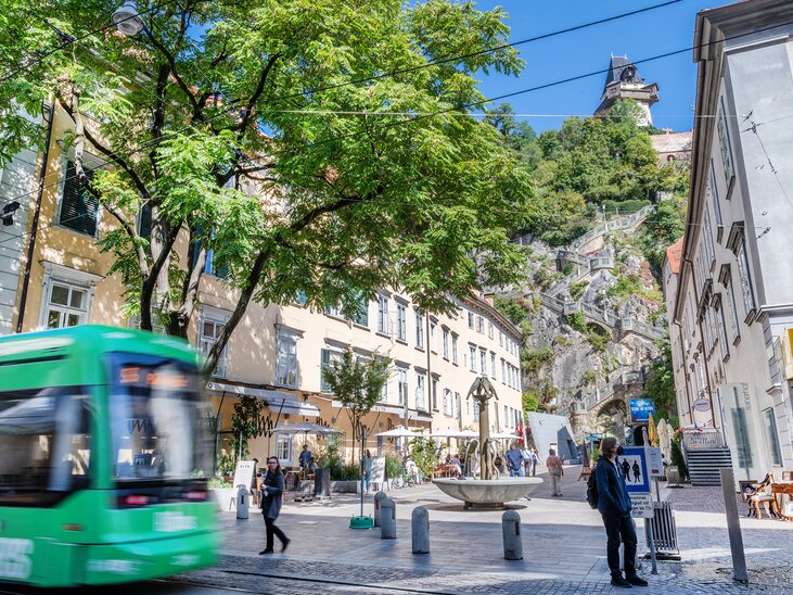 Vibrant scene in Graz, featuring a tram and view of the clock tower. | © achtzigzehn - Hinterleitner