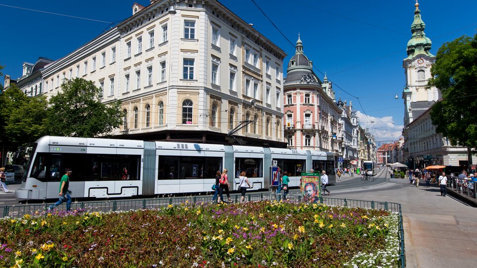 Bunte Blumen und eine Straßenbahn in Graz an einem sonnigen Tag. | © Graz Tourismus - Harry Schiffer
