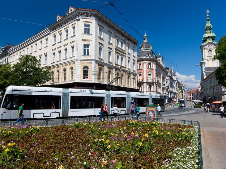 Bunte Blumen und eine Straßenbahn in Graz an einem sonnigen Tag. | © Graz Tourismus - Harry Schiffer