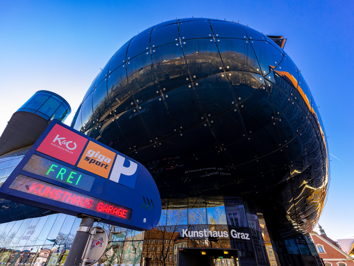 The modern Kunsthaus Graz mirrors its surroundings with a parking sign. | © Graz Tourismus - Harry Schiffer