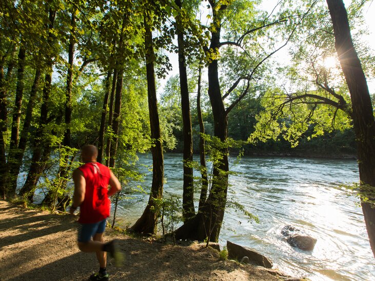 A runner jogs along the Mur River, surrounded by trees. | © Graz Tourismus - Harry Schiffer