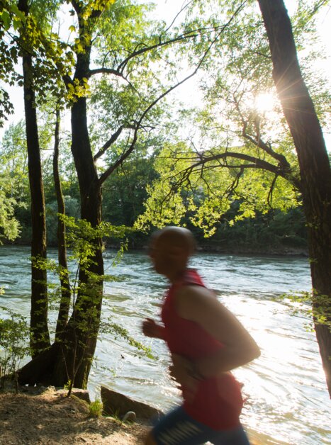 Ein joggender Mann läuft entlang der Mur, umgeben von Bäumen. | © Graz Tourismus - Harry Schiffer