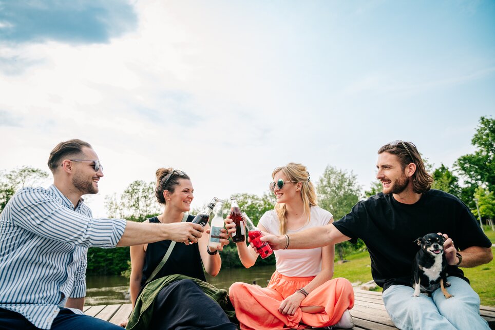Vier Freunde stoßen mit Getränken am Fluß an. | © Graz Tourismus - Mias Photoart