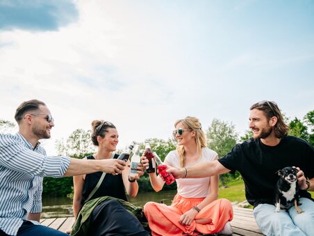 Four friends toast each other with drinks by the river. | © Graz Tourismus - Mias Photoart