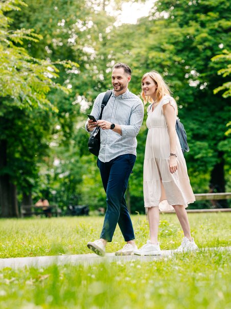A couple strolls through Graz's Augarten park, laughing. | © Graz Tourismus - Mias Photoart