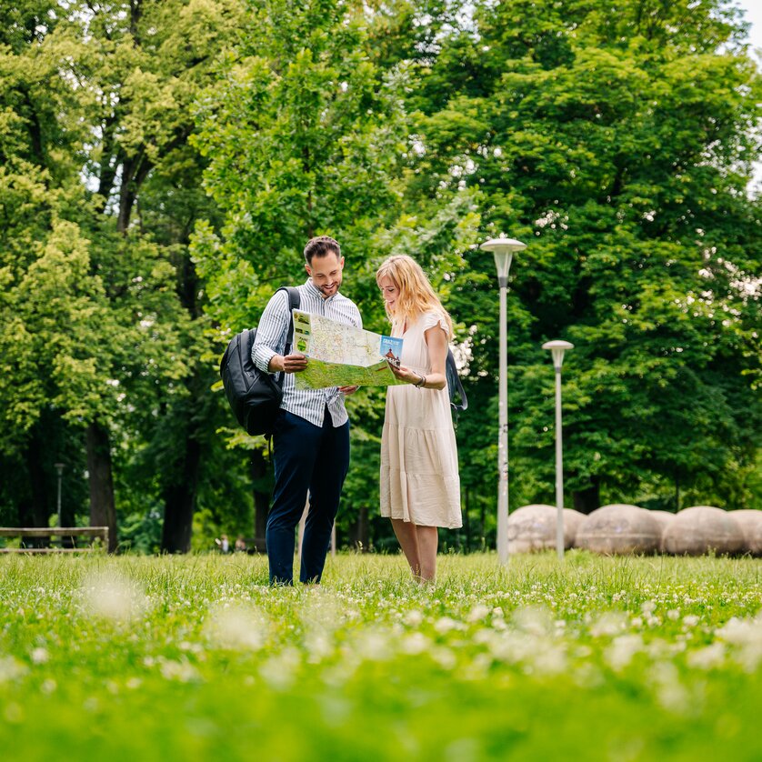 Couple stands in Augarten, looking at a map. | © Graz Tourismus - Mias Photoart