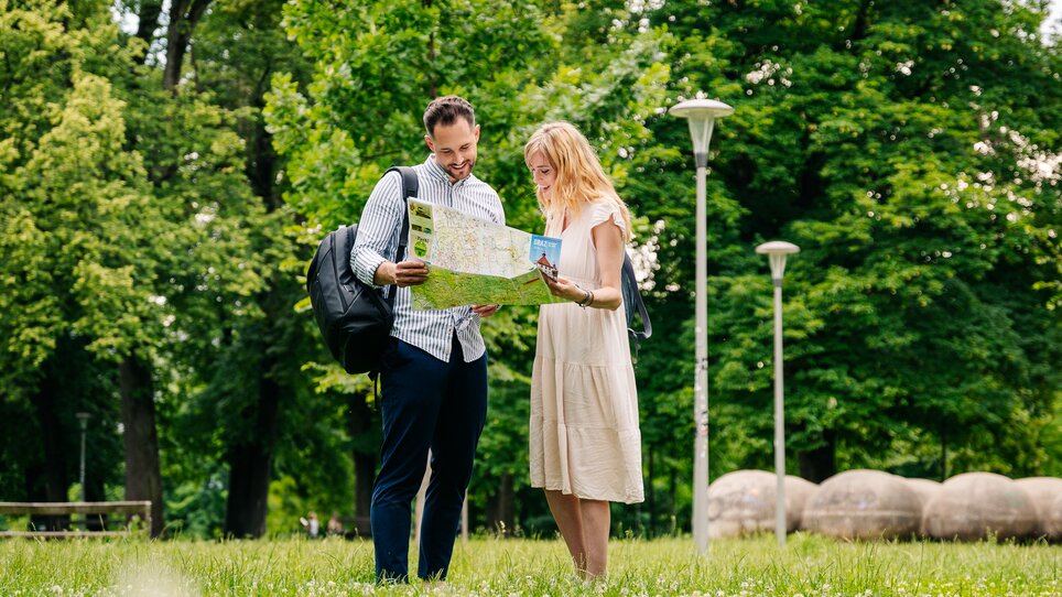 Paar steht im Augarten, schaut auf eine Landkarte. | © Graz Tourismus - Mias Photoart