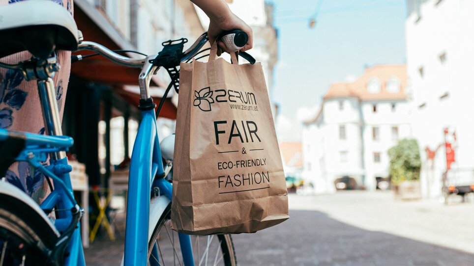Eine Person schiebt ein Fahrrad durch Graz und hält eine umweltfreundliche Tasche. | © Graz Tourismus