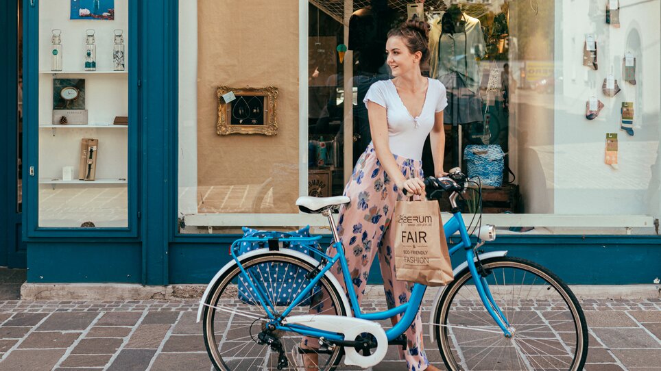 Junge Frau steht neben einem blauen Fahrrad mit einer Einkaufstasche. | © Graz Tourismus