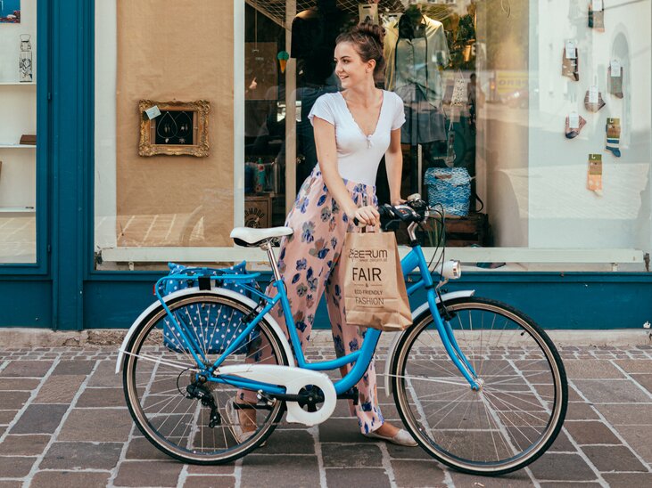 Junge Frau steht neben einem blauen Fahrrad mit einer Einkaufstasche. | © Graz Tourismus