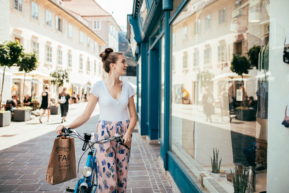 Woman with Bicycle in Graz | © Graz Tourismus A woman in Graz looks into a shop window while holding a shopping bag. | © Graz Tourismus