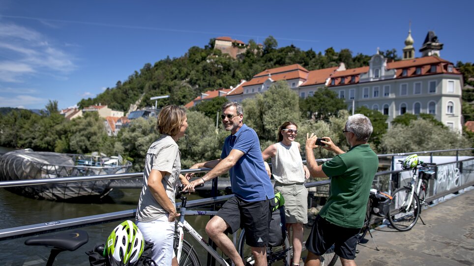 Vier Personen mit Fahrrädern unterhalten sich auf einer Brücke über der Mur in Graz. | © Graz Tourismus - Tom Lamm