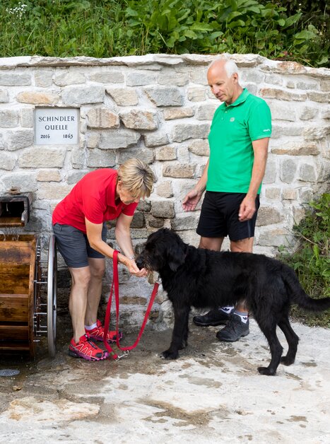 Paar mit Hund an einer Wassertankstelle in der Natur. | © Region Graz - Harry Schiffer