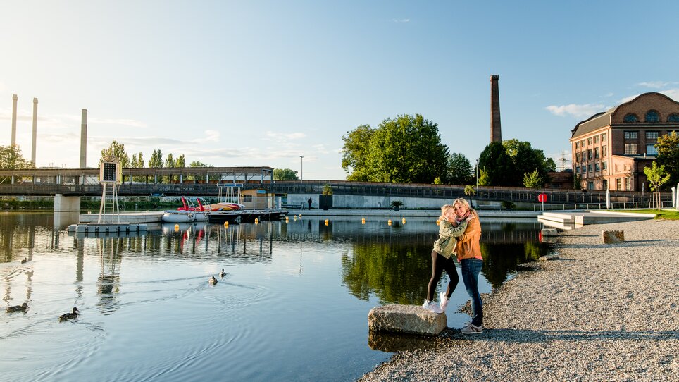 Mother and daughter embrace on the banks of the Mur at the Stadtstrand in Graz during sunset. | © Graz Tourismus - Mias Photoart
