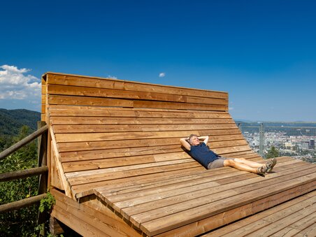 A man relaxes on a wooden lounger with a view of Graz. | © Graz Tourismus - Harry Schiffer