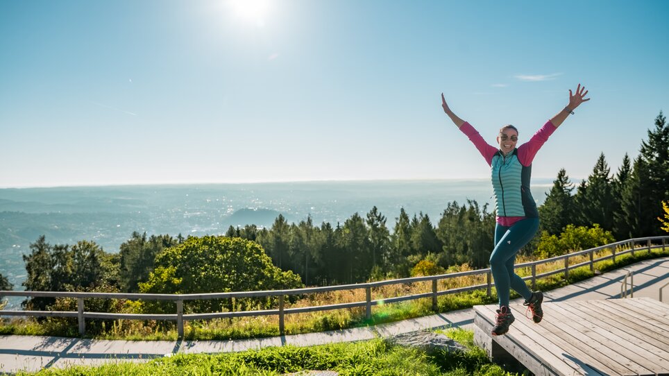 Eine fröhliche Person in der Natur, mit Blick auf die Stadt Graz. | © Graz Tourismus - Mias Photoart
