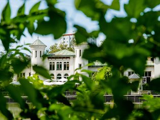 Ein Gebäude am Grazer Hilmteich wird durch Blätter im Vordergrund umrahmt. | © Graz Tourismus - Mias Photoart