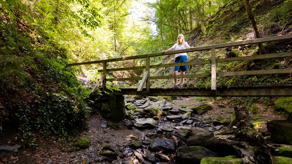 Eine Person steht auf einer Holzbrücke in einer bewaldeten Schlucht. | © Graz Tourismus - Harry Schiffer