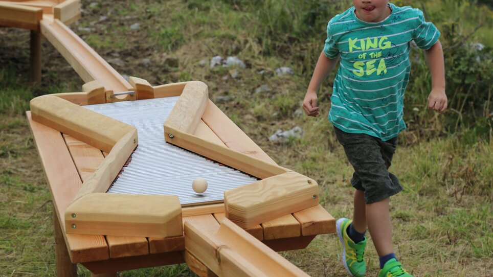Ein Kind läuft fröhlich neben einem Holzspielzeug, das eine Kugel bewegt. | © Holding Graz