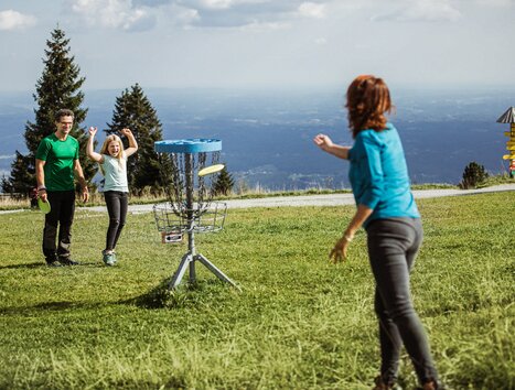 Famiglia che gioca a disc golf al Schöckl con vista sulle montagne. | © Holding Graz - Lex Karelly