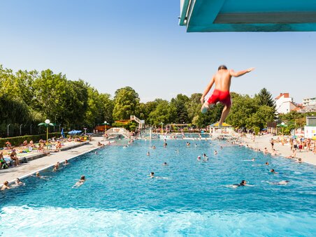 Ein Junge springt ins Schwimmbecken des Augartenbads in Graz an einem sonnigen Tag. | © Holding Graz - Joel Kernasenko