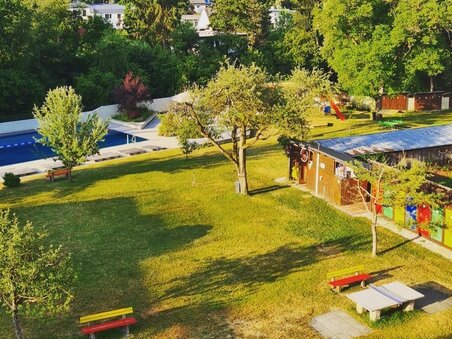 Prato verde con tavoli da picnic e piscina sullo sfondo. | © Ragnitzbad