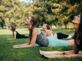 Four women practicing yoga outdoors on grass in a park. | © Graz Tourismus