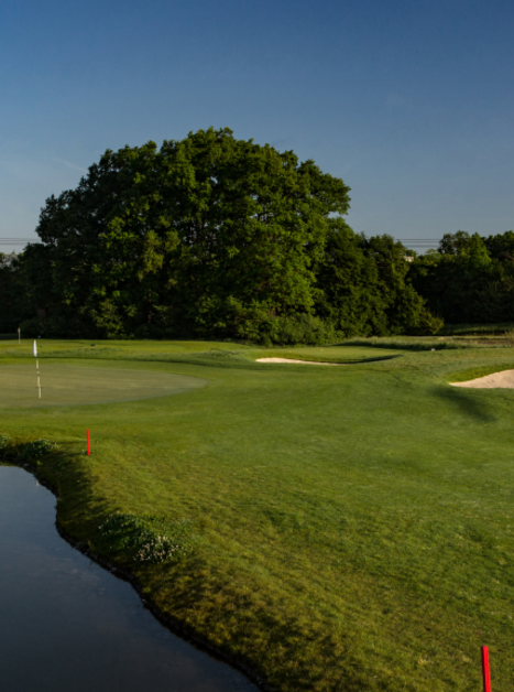 Green golf course with pond and sand bunkers under clear sky. | © GC Grazer MurAuen