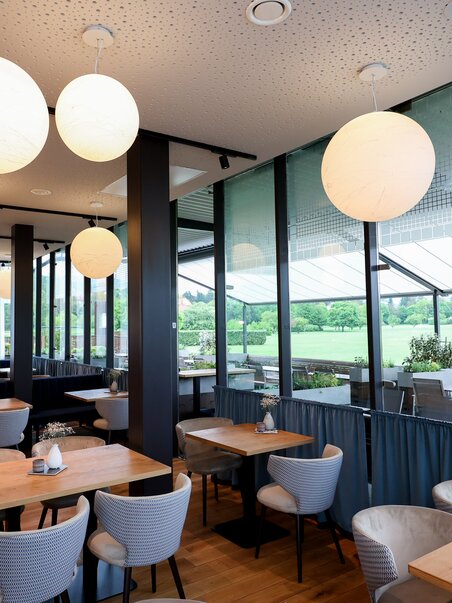 Modern interior of a restaurant with round lamps and view of the golf course. | © GEPA-pictures - Murhof Gruppe