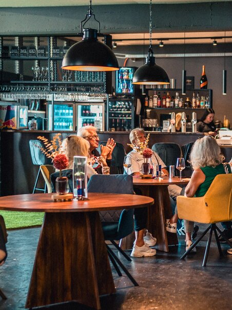 Ein gemütlicher Innenraum mit Gästen, die an einem Tisch sitzen, während ein Kellner bedient. | © GEPA I RUFF Golf Graz