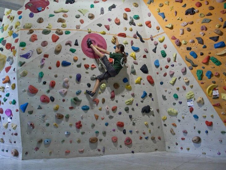 A climber in an indoor climbing gym surrounded by colorful holds. | © CAC