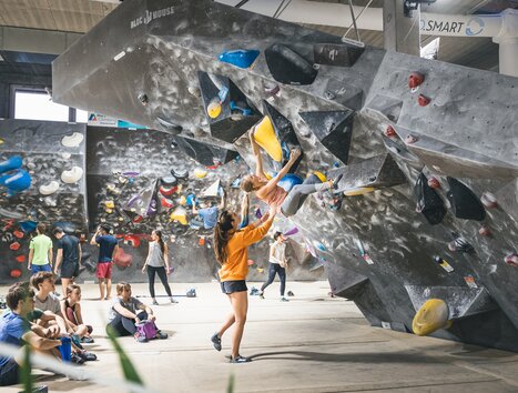 Bouldering in a climbing gym with spectators and trainers. | © byAchimR