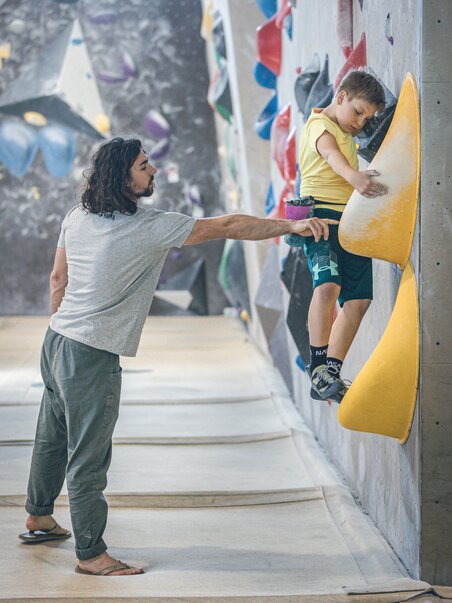 Ein Erwachsener hilft einem Kind beim Bouldern an einer Kletterwand. | © byAchimR