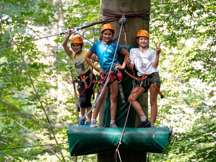 Tre bambini nella foresta di arrampicata con attrezzatura di sicurezza e caschi. | © WAP