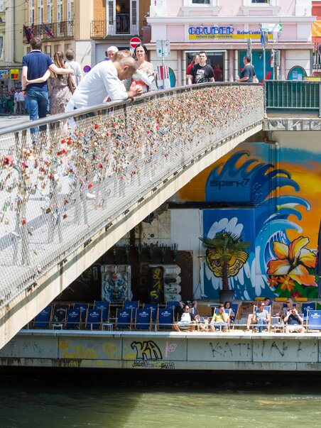 Überblick über die Mur und die bunten Graffitis in Graz, mit einer Brücke voller Liebesschlösser. | © Graz Tourismus - Harry Schiffer