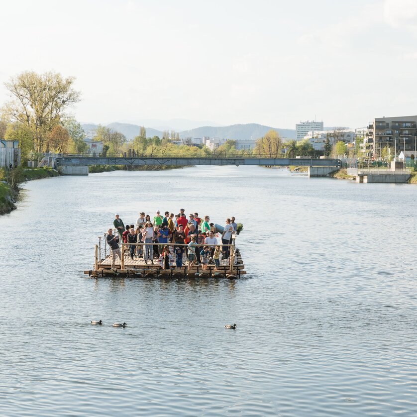 Floßfahren in Graz mit der Flößerei | © LippZahnschirm Gruppe von Menschen auf einem Floß auf der Mur in Graz. Entspannte Atmosphäre am Wasser. | © LippZahnschirm