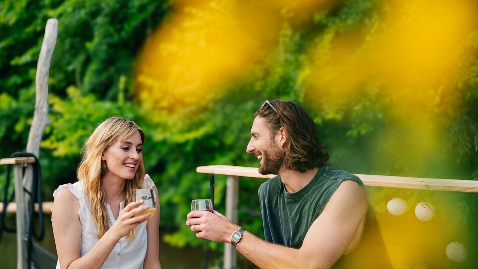 Ein Paar genießt Cocktails in entspannter Atmosphäre beim Floßfahren auf der Mur in Graz. | © Graz Tourismus - Mias Photoart