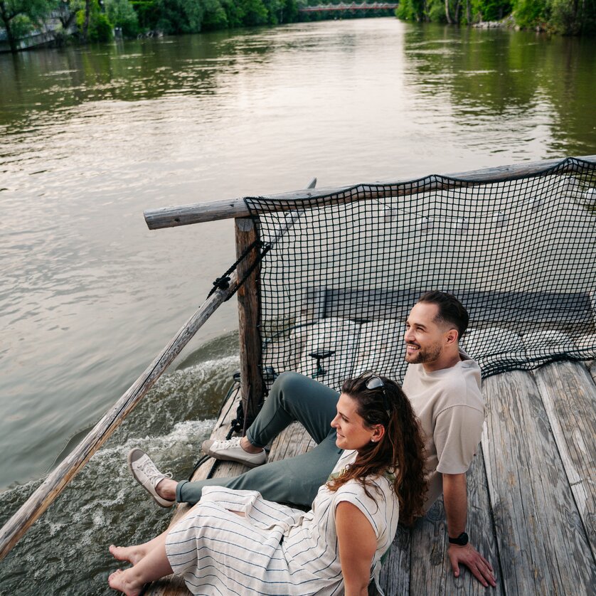 Floßfahren in Graz mit der Flößerei | © Graz Tourismus - Mias Photoart Paar sitzt am Fluss und genießt die Aussicht beim Floßfahren. | © Graz Tourismus - Mias Photoart