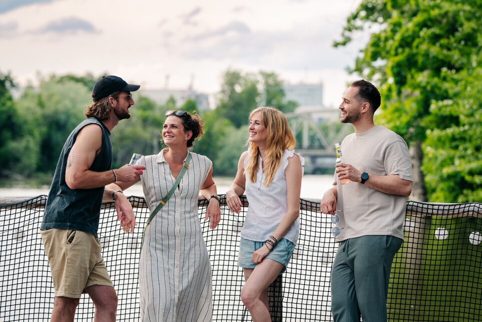 Freunde am Wasser in Graz | © Graz Tourismus - Mias Photoart Vier Freunde stehen auf einem Floß auf der Mur und unterhalten sich. | © Graz Tourismus - Mias Photoart