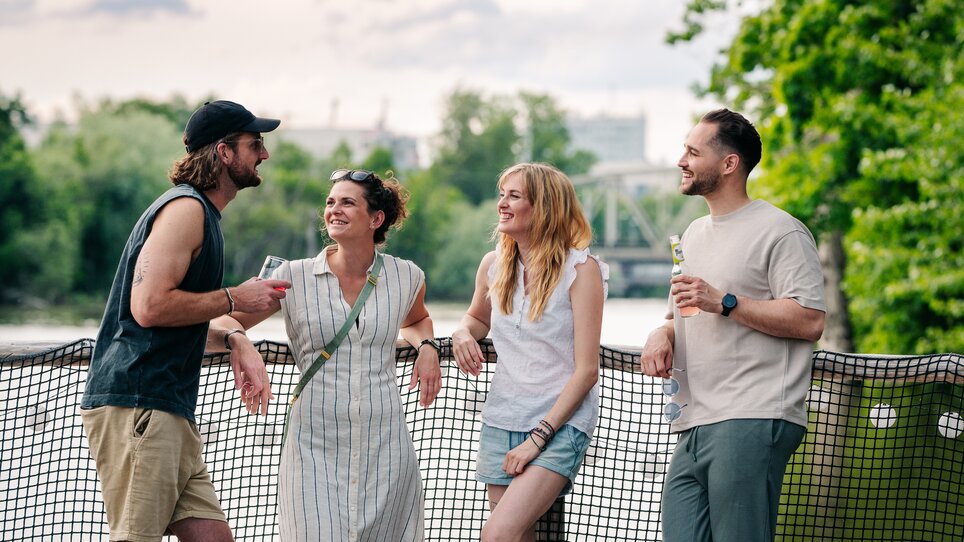 Four friends are standing on a raft on the Mur river and chatting. | © Graz Tourismus - Mias Photoart