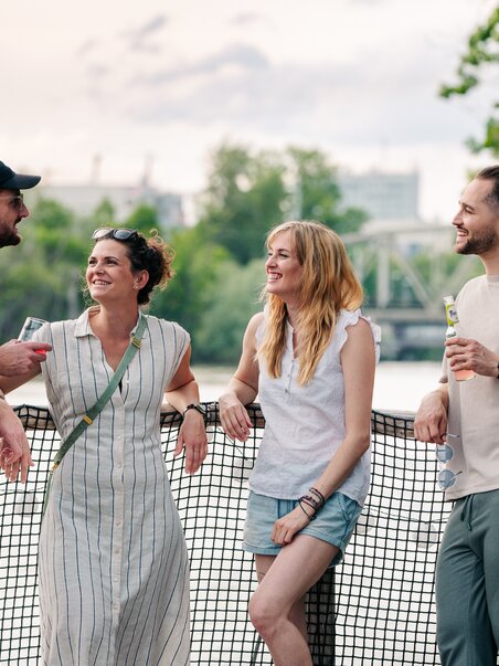 Four friends are standing on a raft on the Mur river and chatting. | © Graz Tourismus - Mias Photoart