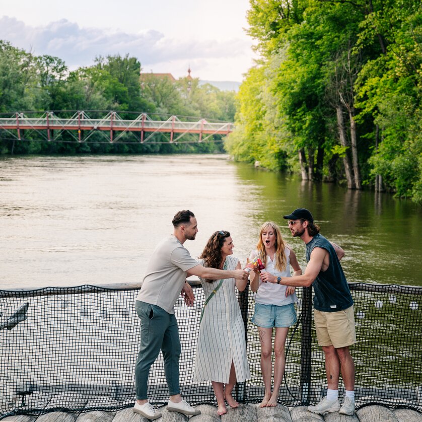 Floßfahren in Graz mit der Flößerei | © Graz Tourismus - Mias Photoart Vier Personen stoßen am Fluss Mur mit Getränken an. | © Graz Tourismus - Mias Photoart
