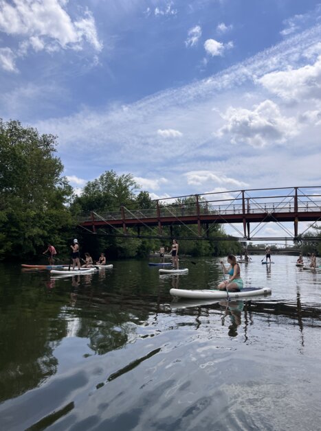 Paddlers sul fiume Mur a Graz davanti a un ponte in una giornata di sole. | © Die Flößerei