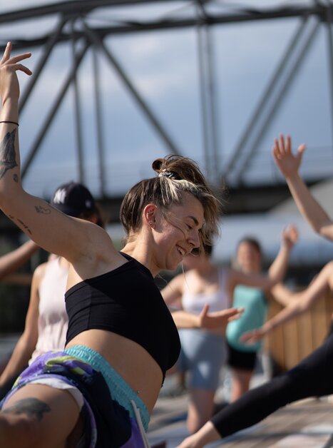 Un gruppo di persone partecipa a un corso di yoga su una zattera sul fiume Mur a Graz, organizzato da “Der Flößerei”. | © Robert Supnig