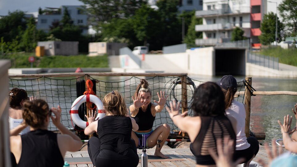 Un gruppo di persone partecipa a un corso di yoga su una zattera sul fiume Mur a Graz, organizzato da “Der Flößerei”. | © Robert Supnig