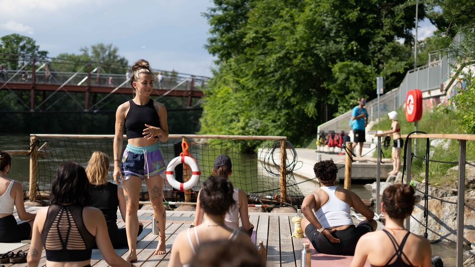 Un gruppo di persone partecipa a un corso di yoga su una zattera sul fiume Mur a Graz, organizzato da “Der Flößerei”. | © Robert Supnig