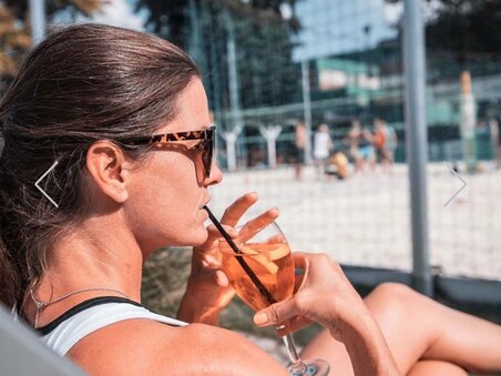 Relaxed woman on the beach volleyball court with a drink in her hand. | © Mur Beach - Ingo Gruber