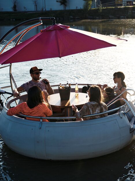 Gruppe von Freunden in einer Murgondel - das ist ein rundes Boot - auf der Mur bei Sonnenuntergang. | © Stadtstrand Graz - Stefan Leitner